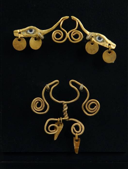 Peru, Two Chavin gold nose ornaments with openwork coils and dangles
One is fashioned from one continuous wire curled into double spirals and twisting into another set of doublle spirals flanking a central suspension plaque and two triangular dangles.  The other has double spirals in the center framed by serpents heads, end to end, each with two suspended circular dangles.   A similar one is illustrated in Oro Del Antiguo Peru, plate 42.
Media: Metal
Dimensions: Height 1 3/4 inches; Width 2 1/2 inches
Price Upon Request
94154
