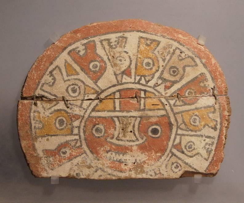 Peru, Early Chancay wood painted circular headdress ornament. with red sun face
A well painted wood disc depicting a sun with serpents heads emanating from the center circle.  The painted surface is stucco-like and in excellent condition. The disc has an ancient repair of a clean horizontal break through the center. There are four attachment holes in the center as well, which implies that it was worn either as a headdress ornament or a pectoral. This is illustrated in CHANCAY.  The Merrin Galleries have illustrated a painted textile with the same sun face motif and emanating serpents on a poster for an exhibition.
Media: Wood
Dimensions: Diameter 9"
Price Upon Request
98089