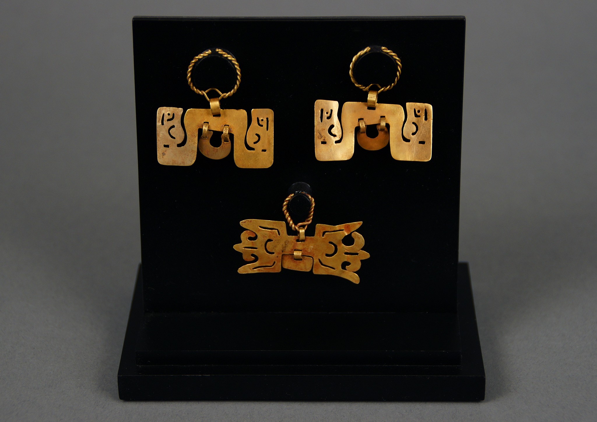 Peru, Chavin Pair of Gold Ear Ornaments and a Gold Nose Ornament with double chevron
The pair of gold ornaments, each with a double headed serpent with cut-out facial details, suspended by a twisted wire loop, and a suspension plaque dangleA gold nose ornament with cutout design and a central suspension plaque. The single nose ornament has a cut-out design sign in an abstract avian face or that of opposing chevrons, suspended by a twisted gold wire loop. pl. 15.
Media: Metal
Dimensions: Widths 1 1/2 inches each; Width 1 3/4 inches
Price Upon Request
94157