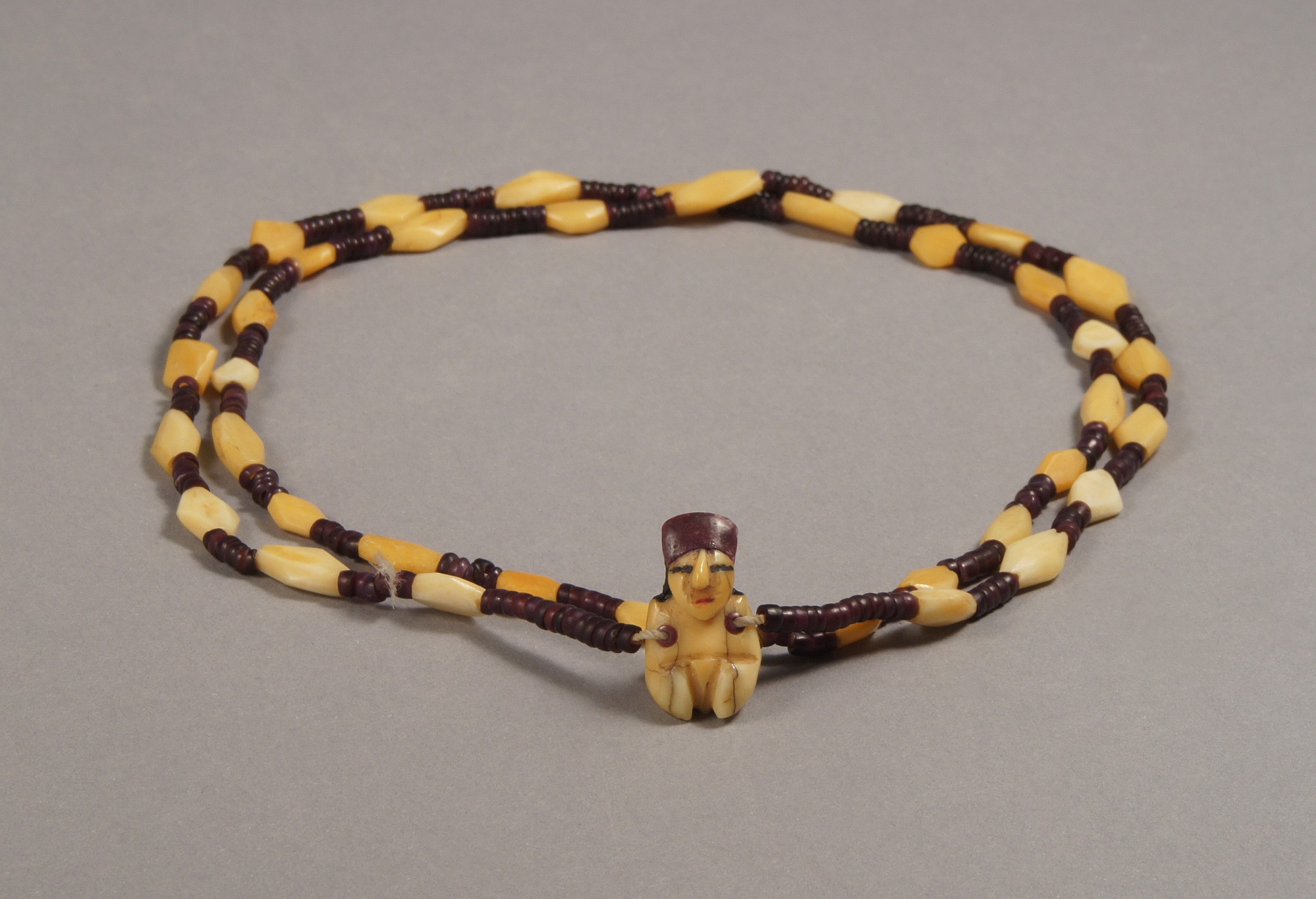Peru, Nazca necklace with bone and syondylus beads and a minature female pendant
The necklace is made of 32 carved bone beads separated by 6 dark purple circular beads. The pendant is a classic Nazca miniature carved female with traces of painted eyes and mouth. The head piece of purple shell is missing. It's possible that the pendant is made up of Whale tooth ivory.  A similar type of figurine is illustrated in 'Miniature Size, Magical Quality - Nasca Art from the Glassell Collection', Marzio, pg 59; and in 'The Inka Empire And Its Andean Origins', Morris and Von Hagen, p.87.
Media: Bone
Dimensions: Length 68 cm.  size of pendant H.1.4cm W. 5cm
$6,500
N1010