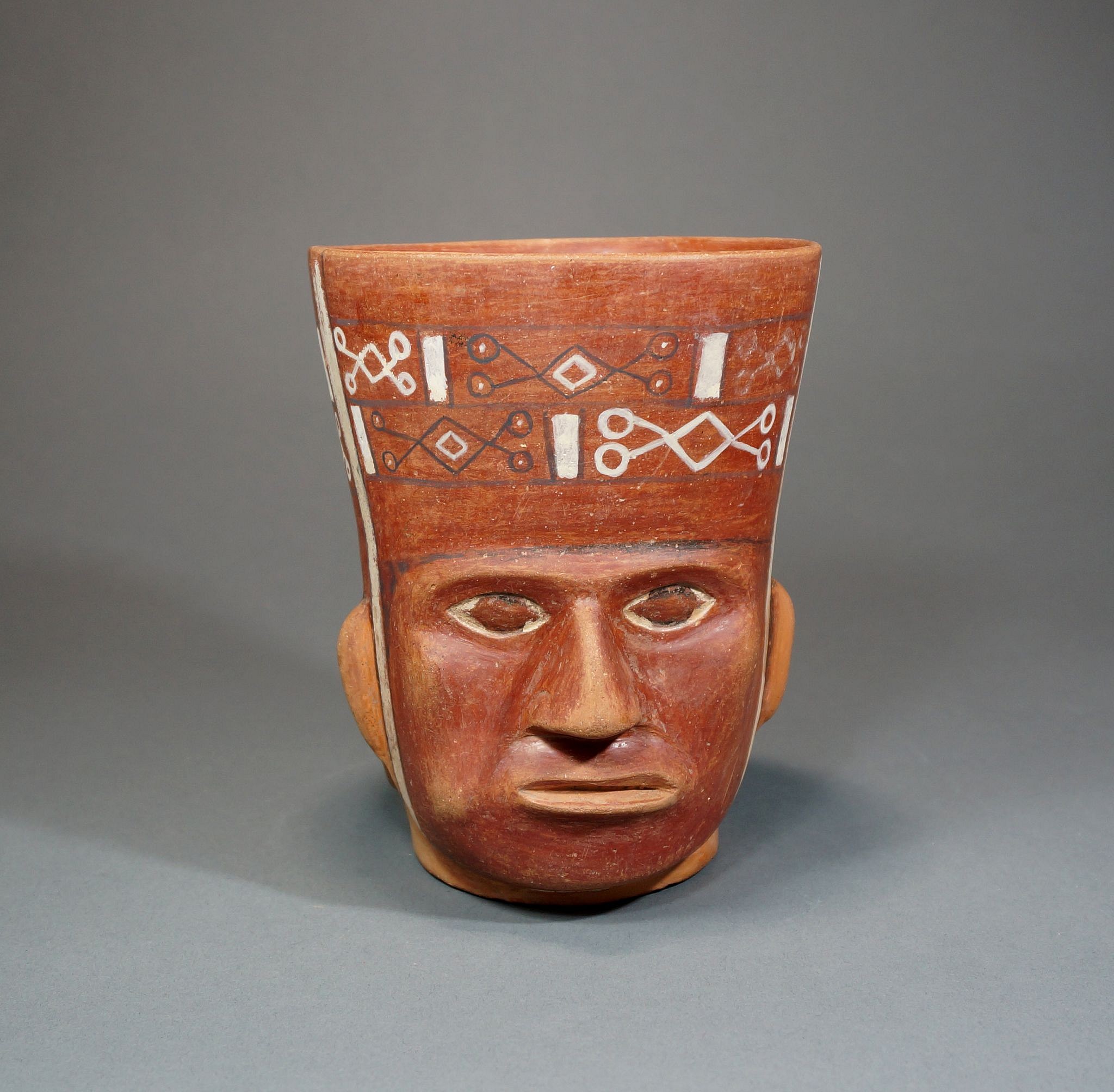 Bolivia, Tiawanaku Portrait Vessel Wearing a Woven Headpiece
This portrait vessel has a modeled coca leaf on the left cheek.  A similar portrait vessel is illustrated in TIAWANKU, ANCESTORS OF THE INCAS, edited by Margaret Young-Sanchez (fig. 5.24).  The portrait vessels from the Tiawanku culture must have been heavily influenced by the Moche People of the coast.  Ex Collection Arthur Sackler prior to 1970.
Media: Ceramic
Dimensions: Height: 5 7/8", Diameter 4 3/4"
n2006