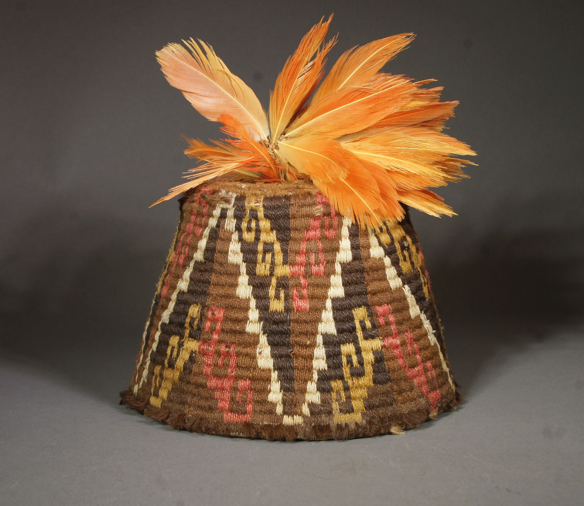 Chile, Inca fez style hat with step design in brown, gold, white and pink and feather plume
A fez style hat was placed as the final adornament on the Inca mummy bundles of Pica, Chile. They were not made anywhere else in all of the Inca Empire.  They were made by a coil method wrapping different colored wool yarns around the coils to acheive the quartered step pattern.  A similar example is illustrated in Arica Diez Mil Anos
Media: Textile
Dimensions: H. 4 1/4 in.hat only  H. with feathers 9"
$5,500
91362