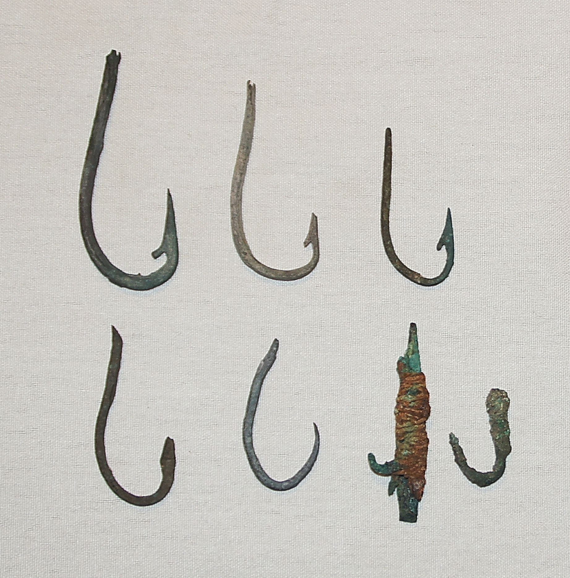 Chile, Late Copper Fish Hooks with Barbs
These barbs were made by hammering and chiseling the copper hooks.  One hook demonstrates how a line was attached to the hook by tying a copper strip around the shaft so it would not slide off.
Media: Metal
Dimensions: Lengths Vary: 1.50" - 2.5”
N6024