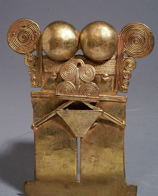 Colombia, Sinú Gold Pectoral of Mushroom Shaman in Trance
Called "Darien pectorals," these ornaments are one of the most fascinating and enigmatic in the corpus of SinÃº gold work. They are not confined to one region, although their greatest concentration is in the SinÃº area of northwestern Colombia, near the border with Panama's Darien Province. They are also found in the Quimbaya region of Colombia further south. The consensus of opinion on these pectorals is that they represent shamans in trance decorated with references to natural psychoactive hallucinogens (Shultes and Bright 1981, Reichel-Dolmatoff 1988). In this work and most such figures, the bell motifs above the face represent hallucinogenic mushrooms, and on some pieces, the mushrooms are realistically represented. Similarly, the mask of spiral curls in front of the face here is a stylized frog with hallucinogenic glands behind its eyes, but in some examples, the frog is completely realistic. Lastly, the vertical spirals on either side of the face are stylized bird wings, since shamans thought of their souls as flying to the otherworld to seek advice and knowledge from the ancestors and deity spirits.
Period: Colombia, Sinu, Northern Region, c. AD 400 - 1500
Media: Metal
Dimensions: Height: 4 1/2" x Width: 3 1/2"  Weight  119 grams
Price Upon Request
M7027