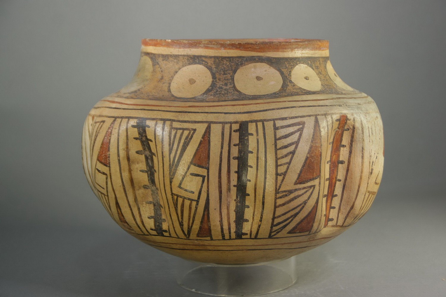 Mexico, Casas Grande Gadrooned Ceramic Vessel with Geometric Designs
This unusual ceramic bowl has nine fluted sections separated by symbolic cacti imagery.  The bowl is painted with red and black geometric designs on a beige ground.  On the bottom are three large concentric black lines.  It has a tapered neck that is decorated with nine beige circles on a black ground.  Each circle has a central black dot, which symbolizes an aerial view of a cactus.  This vessel originates from Casas Grande, a site located in the Mexican state of Chihuahua, along the Casas Grande River and South of the US Puebloan ruins.  A good reference is “Casas Grandes and the Ceramic Art of the Ancient Southwest” by Richard Townsend, published by the Art Institute of Chicago.  The bowl is in good condition with one crack on the bottom restored and a small hole on one of the fluted sections.
All parts original.
Media: Ceramic
Dimensions: H. 6" x W. 8"
$2,900
n2046