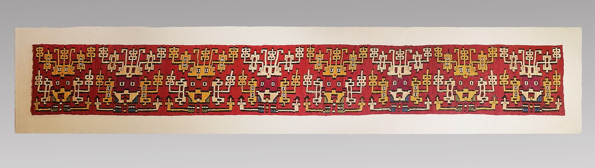Peru, Nasca Slit Tapestry Band with 8 Faces of The Proliferous Being on Red Ground
All eight faces are in the same orientation and alternate between two color arrangements: those with burgundy faces and those with red-orange faces.  Each of the faces has a headdress with extensions, a mouth mask with extensions, and fingers holding a horizontal staff.   One of the few Nasca tunics which depicts similar face bands and is same width is illustrated in TEIDOS MILENARIOS - ANCIENT PERUVIAN TEXTILES by Jose De Lavalle, page 264-5, ISBN# 9972-717-01-1.
Media: Textile
Dimensions: Lengtht: 45 1/2" x Width 6"
Price Upon Request
M6039