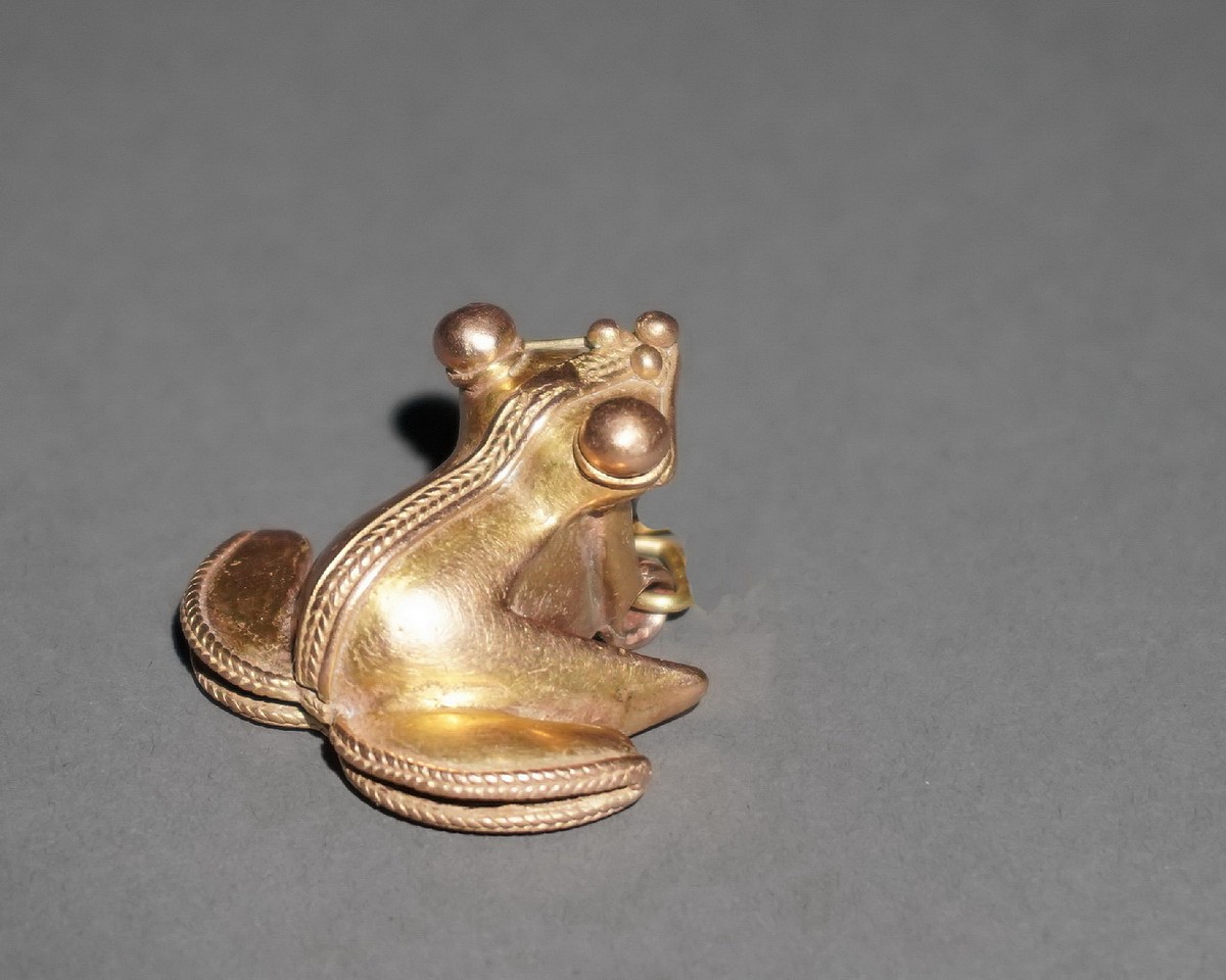 Colombia, Tairona Gold Cast Frog Pendant with Rattle
This expertly crafted gold pendant depicts a frog hunched on its back flippers. The frog has spherical eyes and a delicate braided ribbon that slopes down its back and borders its flippers.  There is a modern suspension loop hung from the original suspension arrangement.  Jan Mitchell collection prior to 1970, by descent to his sons.
Period: Colombia, Tairona, Santa Marta c. AD 1000 - 1500
Media: Metal
Dimensions: Length: 1 7/8" x Width: 1 5/8"  Weight: 21.2 grams
Price Upon Request
p1045b