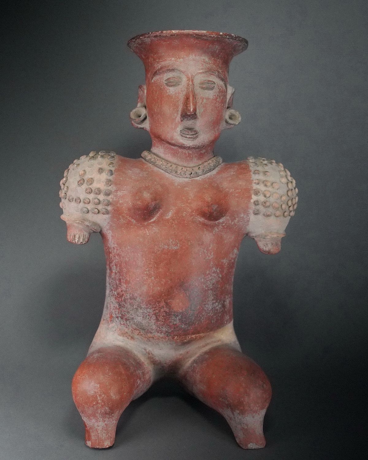 Mexico, Colima Seated Ceramic Sculpture of a Female
This seated female wears a necklace and earspools.  She is adorned with shoulder pellets and has short arms that end with stubs in place of hands.  The pellets may represent armor intended as protection for a person with short arms.  Female figures in Pre-Columbia may have been linked to concepts of the earth and fertility and are thought to represent initiated women ready for marriage and childbirth.  Usually, these figures appear to be disengaged from daily life.  Similar style Coahuanyana Valley figures are in the collection of the Fowler Museum at UCLA, and The Arizona State Museum of Natural History.  Ex-collection Hiroshi Miura, Tokyo, Japan acquired prior to 1970's.
Media: Ceramic
Dimensions: Height: 15.5"(38cm) x Width: 10"(22cm)
$5,400
p1055