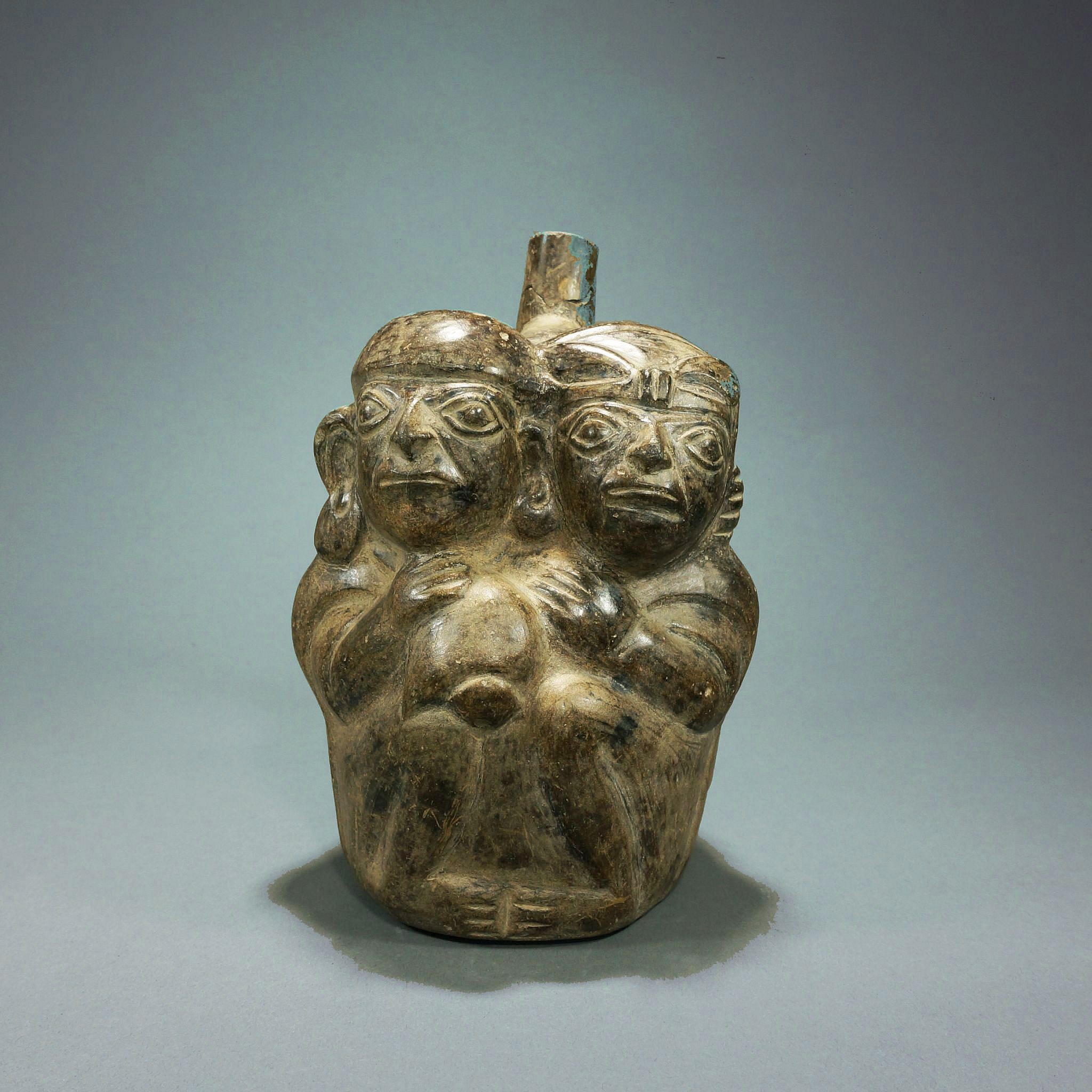 Peru, Moche II Grayware Vessel with Embracing Couple
An embracing couple is an extremely rare subject for Andean art from any culture.  Although ancient Andean art features many human characters such as hunters and shamans, as well as semi-human deities with a wide range themes and emotions, romantic couples are not a common theme.  In this sculptural depiction of a Moche couple, the male wears large ear ornaments, and holds a conch trumpet, and the female wears a feather plume in her hair, all signs of wealth and status.
Media: Ceramic
Dimensions: Height 8"
Price Upon Request
M9015H