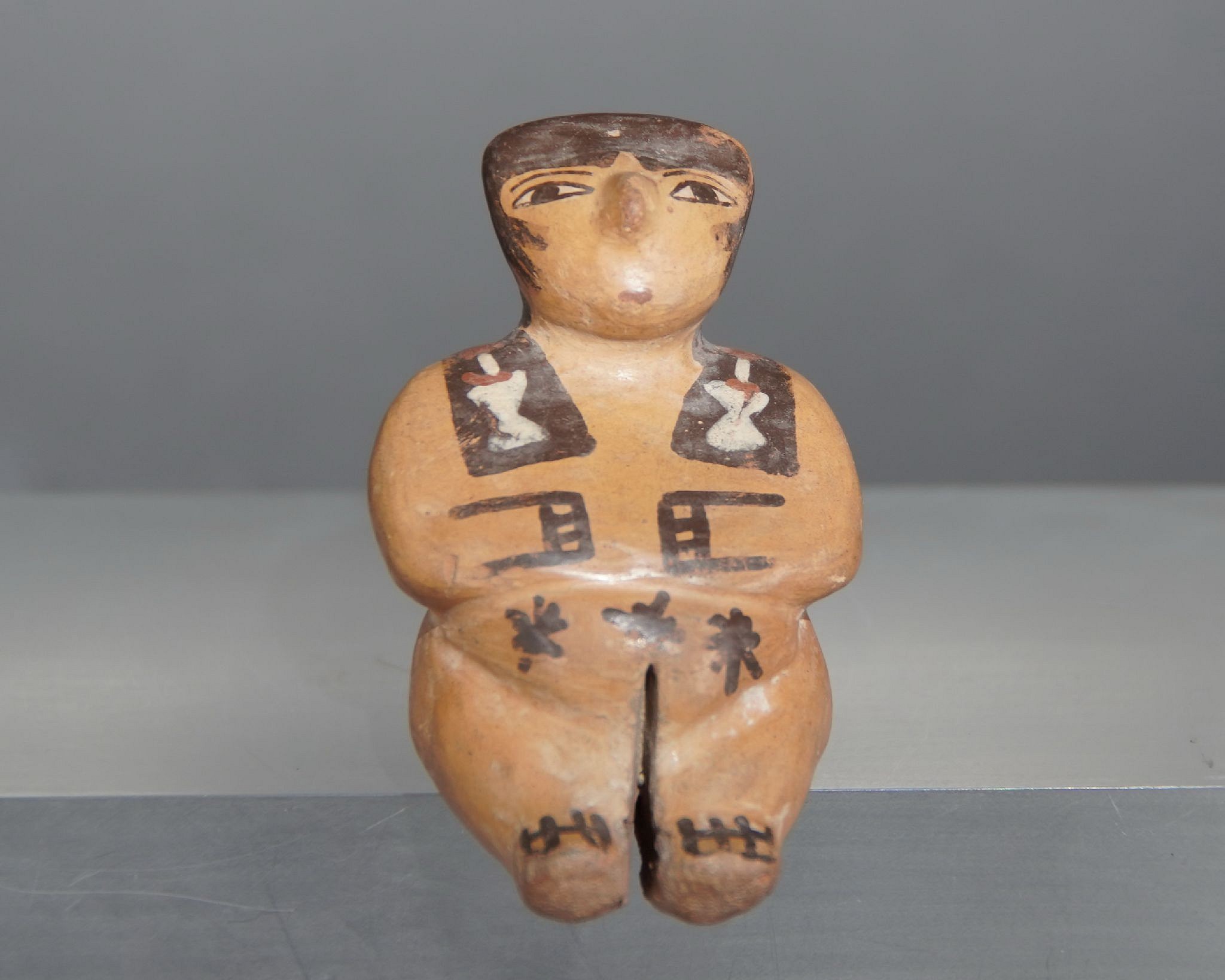 Peru, Nasca Miniature Female Seated Figurine
This seated ceramic female has hands painted on her belly, black hair painted falling over the shoulders, white hair ornaments, and tattoos painted on each buttock.  The intricate tattoos depict the San Pedro cactus, which is known to have psychoactive properties.  The archaeological record indicates that San Pedro cactus was likely used by the ancient Andeans as a libation during shamanic ceremonies.  This figurine would originally have been dressed in a miniature woven garment, which was eroded or lost over time.  A similar figure is illustrated in A Sourcebook of Nasca Ceramic Iconography, p. 146.  Ex. collection Jean Lions, France.
Media: Ceramic
Dimensions: Length: 7.1cm
$2,500
M4049