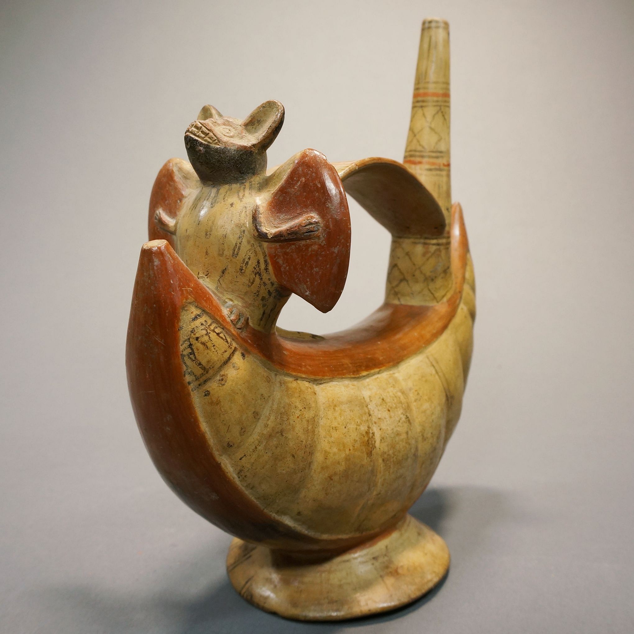 Peru, Lambayeque Whistling Vessel with Bat Atop Pacay Fruit
This ceramic bridge-spout whistling effigy vessel was crafted in the shape of fruit bat resting atop a Pacay.  The Pacay fruit, found in the Amazon, is related to mangoes and guavas.  Fruit bats have an extremely good sense of smell and sharp teeth with which to open the tough skins of fruits.  The whistle built into the vessel, customary for Lambayeque vessels, is seen just behind the bat.  Bats are a rare motif and quite meaningful in ancient Andean mythology as they are associated with transport to other worlds.  The vessel was painted with orange slip and black octopus ink on a buff ceramic ground.  There are only two other known Lambayeque vessels with sculptures of bats, one is illustrated in "Ceramics of Ancient Peru" by Christopher Donnan, 1992, p.89, and the other is the property of The American Museum of Natural History.
Media: Ceramic
Dimensions: Height 8" x Length 6 1/2"
Price Upon Request
mm145