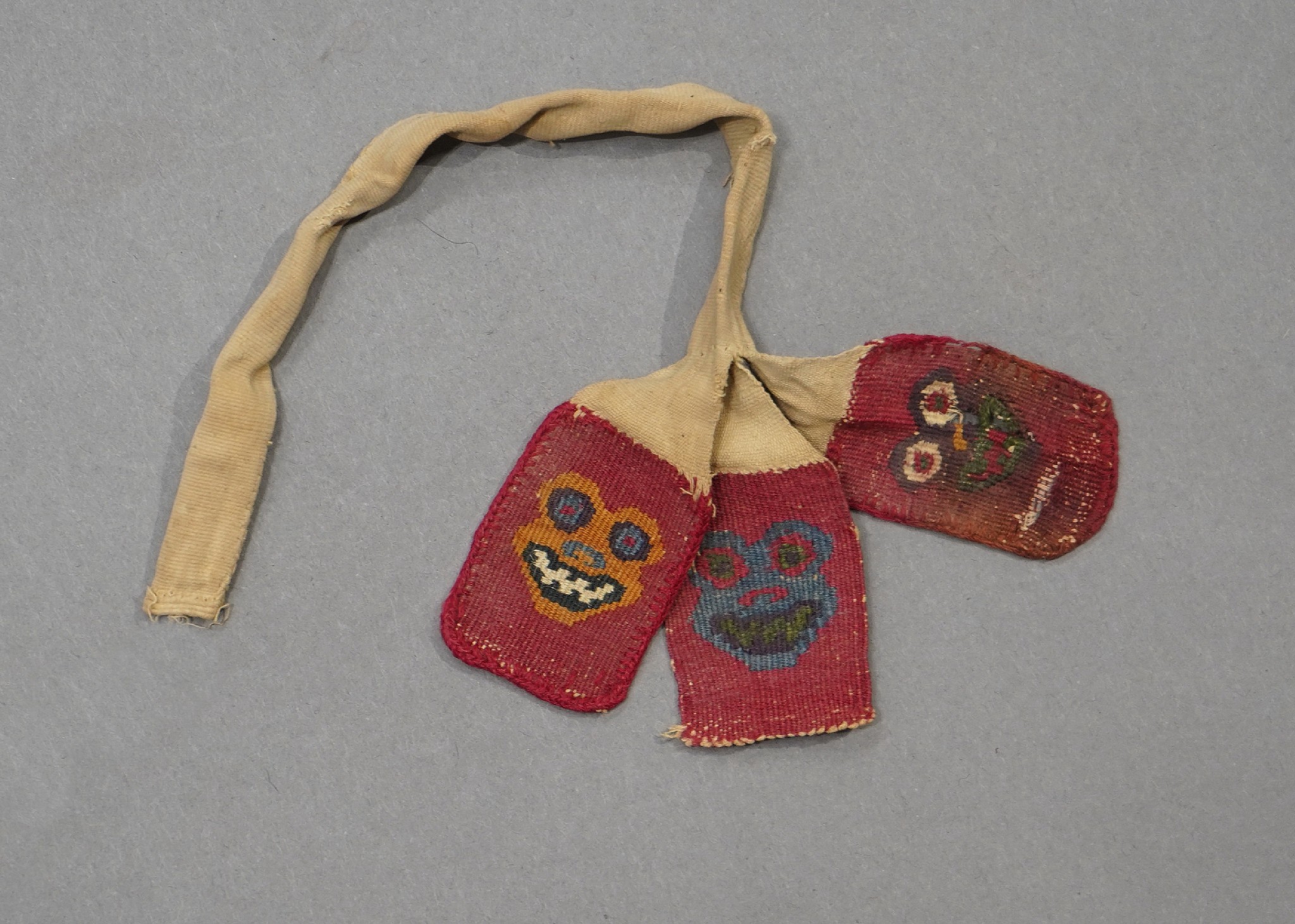 Peru, Three Wari Woven Tabs with Animal Heads
These woven tabs with stylized grinning toad faces were once part of a sash. The tabs are woven in orange, green, blue, white and black on a red ground.  A similar set of tabs is illustrated in Animal Myth and Magic,by Vanessa Moraga,  p. 110.
Media: Textile
Price Upon Request
91095a