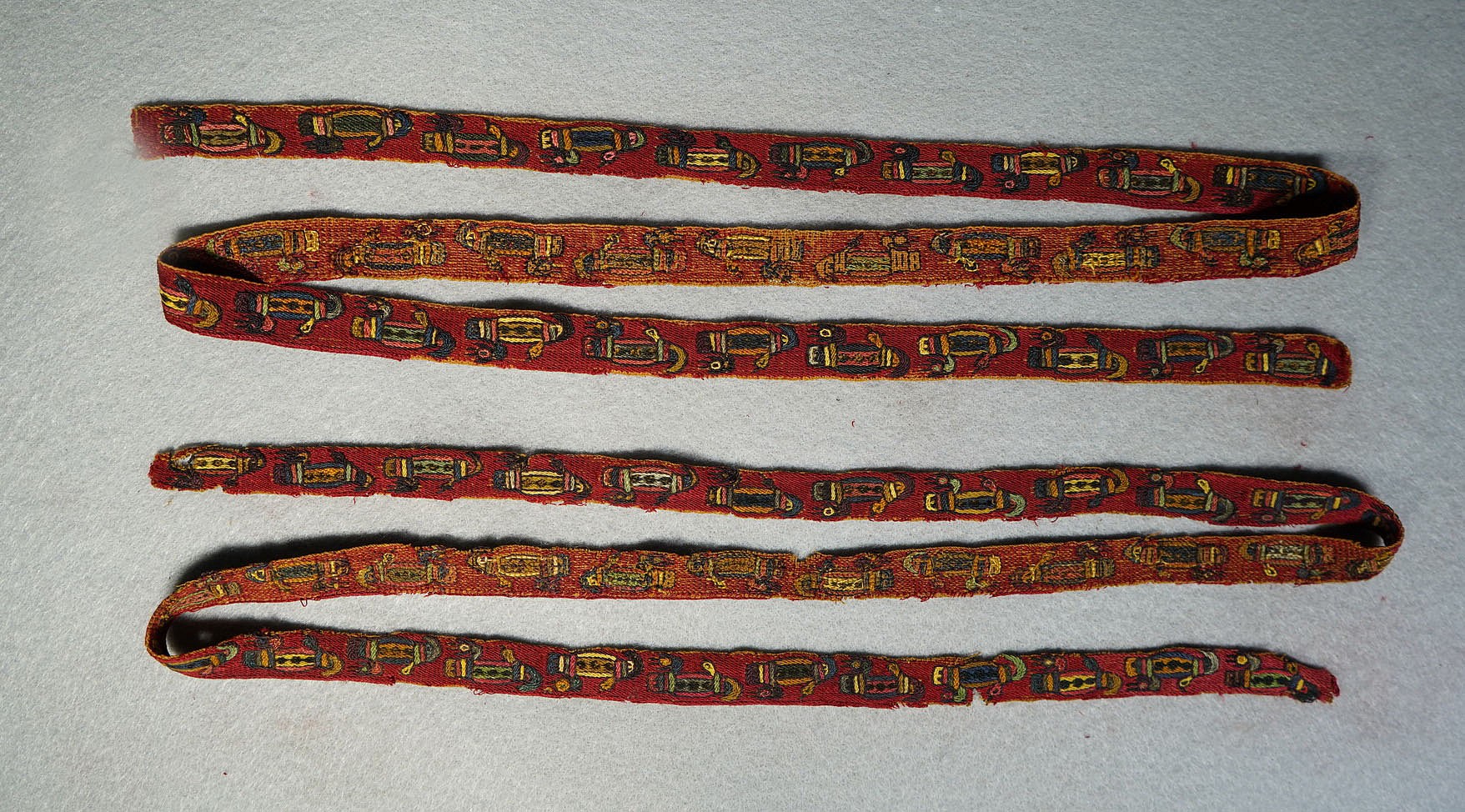 Peru, Pair of Proto Nazca Embroidered Borders with Duck Motif
Weaving technique: embroidery.
These colorful borders to a headpiece were woven with a continuous duck motif in alternating colors on a red ground.  When held vertically, the images of ducks appear to be monkeys with faces turned forward, hands held up, and tails curving outward. The weavers used elemental plied wool embroidery, woven with colorful threads through a plain weave of undyed cotton ground fabric. Acquired in 1991 from a California collector prior to the 1980s. Unmounted.
Period: Peru, Proto-Nasca, South Coast, c. 300 - 100 BC
Media: Textile
Dimensions: Lenght: 40" x Width: 12 1/2" each
$2,000
91263