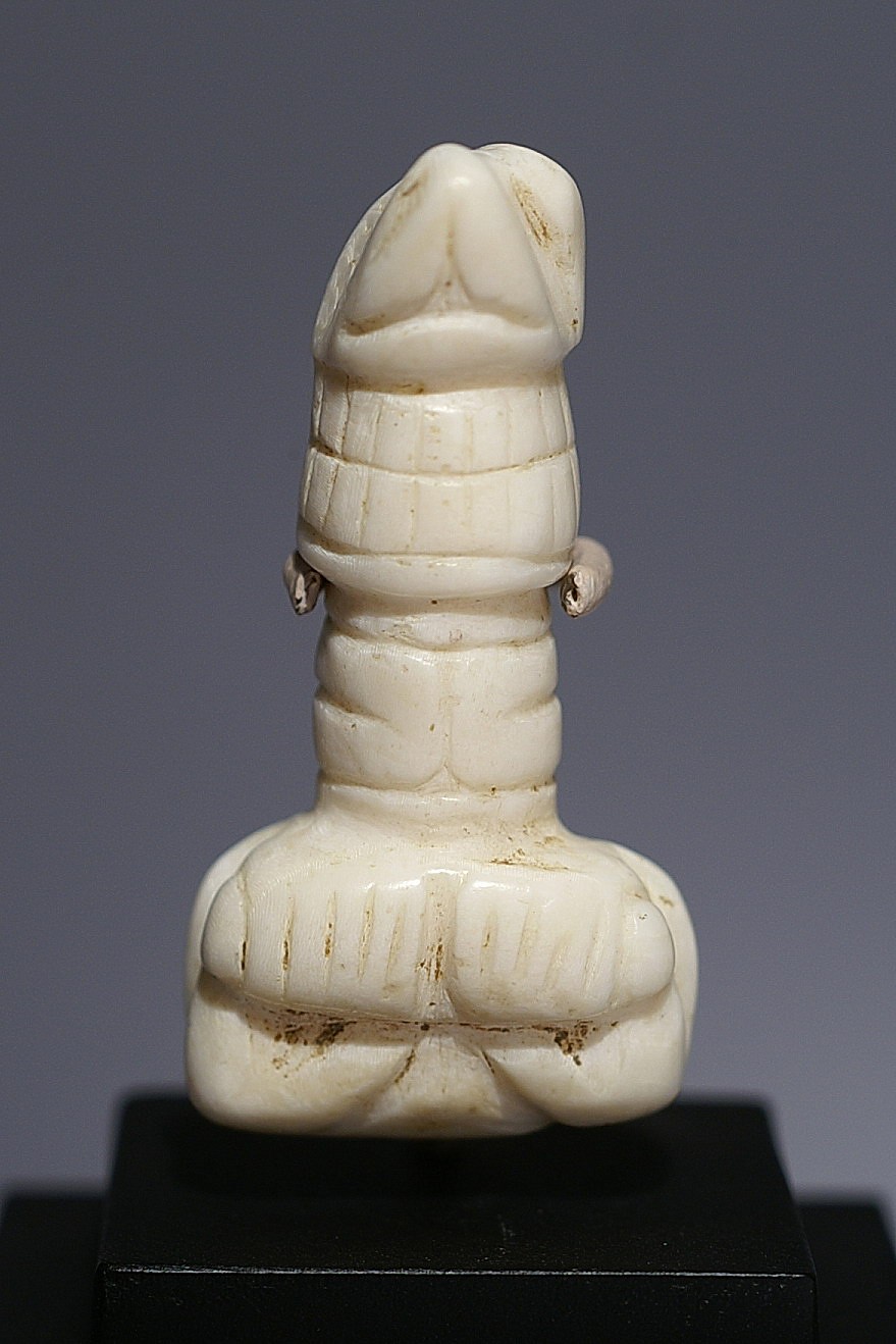 Dominican Republic, Taíno  Shell Amulet of Long-necked Deity
This highly abstract and unusual carving is made from one piece of shell.  This deity has a bat-like nose, large teeth in a wrap-around grin, a long neck, and arms folded over the chest. The legs contort in a forward curl terminating in prominently featured incised toes.
Period: Dominican Republic, Taíno , Early Classic Period, c. AD 600 - 1000
Media: Shell
Dimensions: Height:  1 3/8"
98424