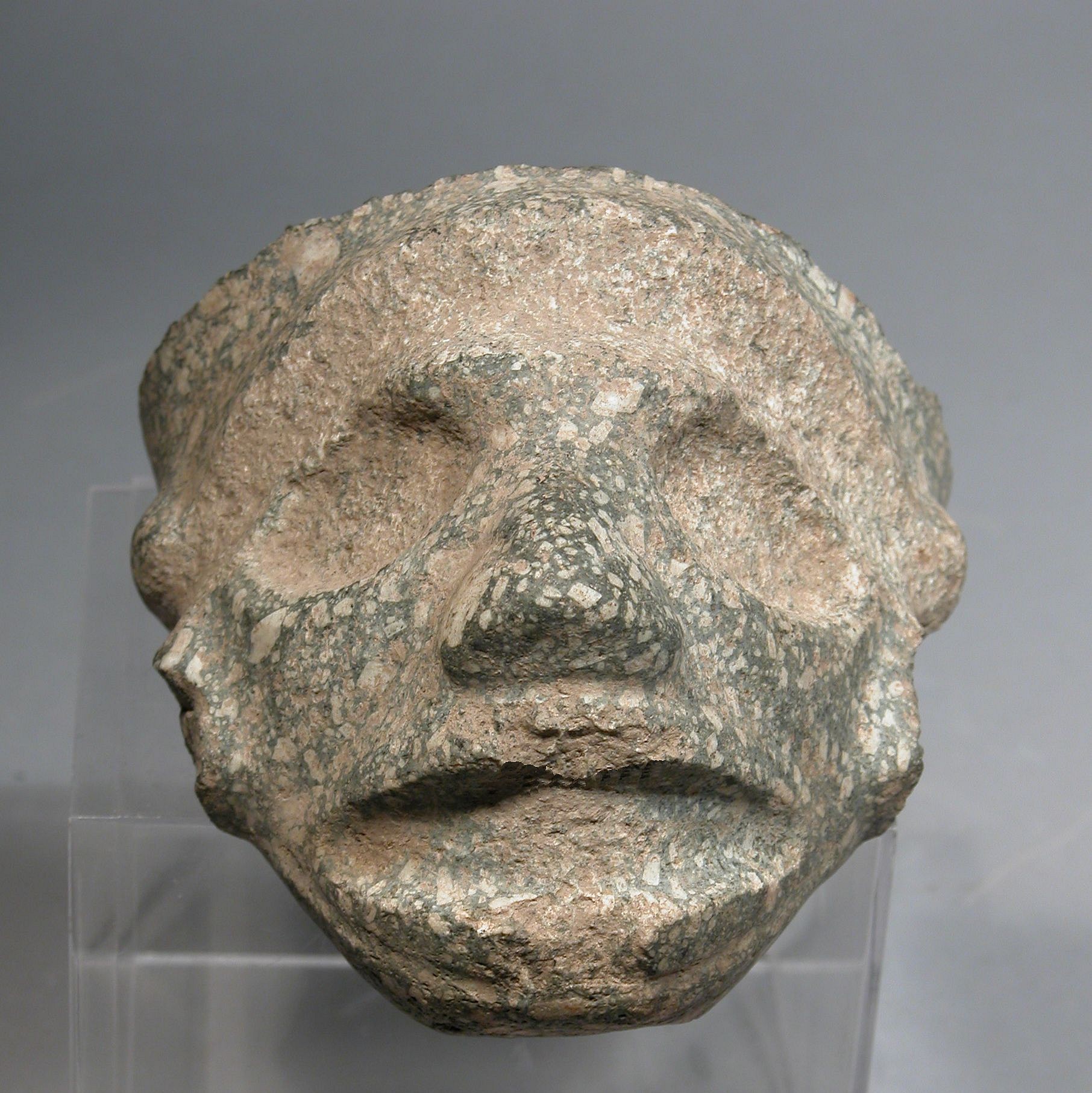 Dominican Republic, Taíno  Stone Face to a Large Three-Pointer
This face is likely a fragment of a large three-pointer that was carved from speckled granite.  The face is of the classic crowned style that most likely represents of the agricultural deity Yucahu, the supreme deity associated with the cassava harvest.  The Taíno valued broken works, especially those believed to be endowed with a spiritual essence.  A very similar fragment from Puerto Rico is in the Smithsonian Museum’s archives.  This example is good for understanding how hard stone zemi were crafted, based on the view from the “killed” back. 
Period: Dominican Republic, Taíno , c. AD 1000 - 1500
Media: Stone
Dimensions: Length from chin to forehead: 5 1/4" Width from ear to ear: 6 1/2"
99208