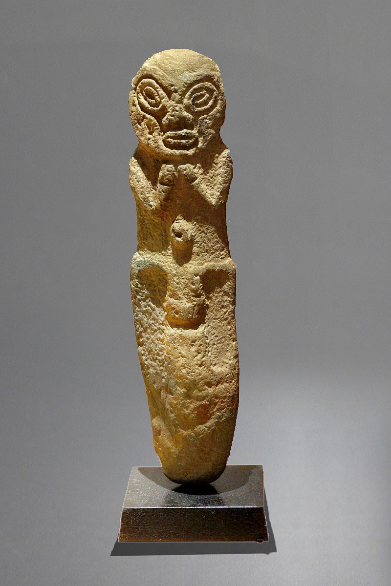 Dominican Republic, Large Taíno Carved Stone of a Deity
This deity has large, deeply carved, stylized eyes below an arched brow.  His chin rests on arms held closely to his chest, and he sits on his haunches, with knees pointing forward and toes pointing downward.  This classic contemplative pose appears in many early Taíno  figurative sculptures, and is suggestive of the deity Baibrama, who symbolizes healing, renewal, and verdant crops.  At the navel area is a protruding bellybutton, indicative of fertility.  The prominent navel appears often as a theme in stone Pre-Taíno  art. The bottom of the statue has been worn to a smooth taper for the purpose of setting the statue into the ground.  Stone carvings taller than 15â€ are rare in Taíno  art.  The stones used by the Taíno  to craft large figures were speleothems - rock formations found in caves, usually composed of limestone or dolomite.  Most of these figures were used as perimeter markers that lined the ball courts of ancient Taíno  centers in Puerto Rico and the Dominican Republic.  Many of these figures are still in situ at archaeological sites with ball courts, such as Caguana (Puerto Rico) and the Corrado de los Indios (Dominican Republic).  There are known carvings in caves in the region with similar facial features.  The Metropolitan Museum of Art has a similar figure carved of sandstone.
Period: Dominican Republic, Taíno , c. AD 1000 - 1500
Media: Stone
Dimensions: Height: 23 5/8"
M7105