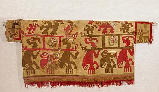 Peru, Tapestry Shirt with Anthropomorphized Pelicans Carrying Manta-Ray Deity
This tapestry woven shirt with short sleeves was crafted with cotton warps and camelid wefts in red, brown, olive green and white on a yellow-ochre ground. The backs of the panels display the same scene in reverse colors.  The elaborate ritual procession portrayed by this textile was likely the result of an entheogen-induced vision seen by a highly skilled shaman or artisan. A manta ray deity, identifiable by his tail and large, flat eyes, is elevated on a litter carried in exaltation by anthropomorphized cormorants. Litters were a prestigious mode of transportation along the North coast of Peru, indicating the
importance of the manta deity. Large manta rays live in the waters off the Pacific coast of South America, and these marine animals are extremely beautiful and majestic. A small brown pelican appears to imbibe a psychedelic brew, while the poles that make up the litter transform into eels &ndash; revered in Andean mythology for their ability to transition between land and sea. This imagery would have been extremely important to the Pre-Columbian psyche as their survival was contingent upon the appearance of healthy manta rays and pelicans. Rays feed upon plankton and other small marine life. These smaller life forms carried by the ocean currents would die off during disastrous climatic events such as El Ni&ntilde;o. The sight of a healthy manta ray along the coast would be a cause for celebration as mantas were an indicator of the return of a prosperous fishing season. Pelicans are equally crucial to the Peruvian ecosystem. They are excellent fishers and produce valuable guano (fertilizer; in the Chimu&rsquo;s animistic worldview, the appearance of pelicans would have been a harbinger of prosperity. The return of the manta-ray together with the pelicans signals the health of the biosphere, and an abundance of fish for both the pelicans and the human population. A healthy ocean was a cause for festivities. This tunic was formerly in the collection of the Southwest Museum outside of Los Angeles. It is illustrated in Ann Rowe&rsquo;s Costumes and Featherwork of the Lords of Chimor. Acquired in 1995 from a New York gallery. 

Media: Textile
Dimensions: Width 47-1/2" x Length 19-1/2"
Price Upon Request
96127